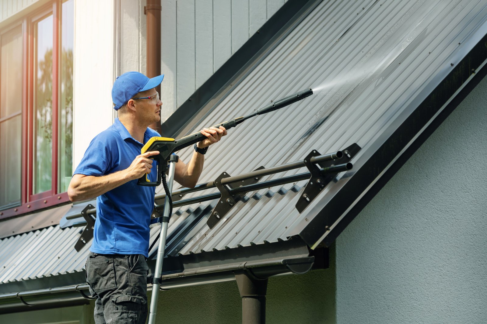 Technician cleaning black roof streaks from asphalt shingles on a residential home