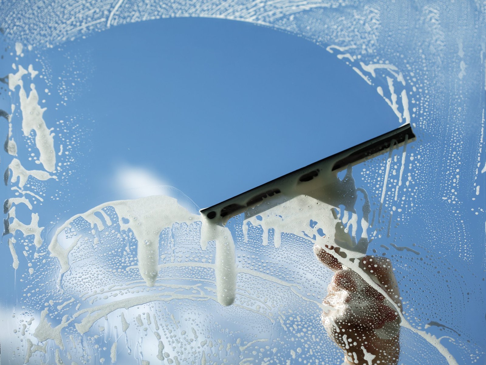 Experienced cleaner removing water spots from exterior glass with professional window tools
