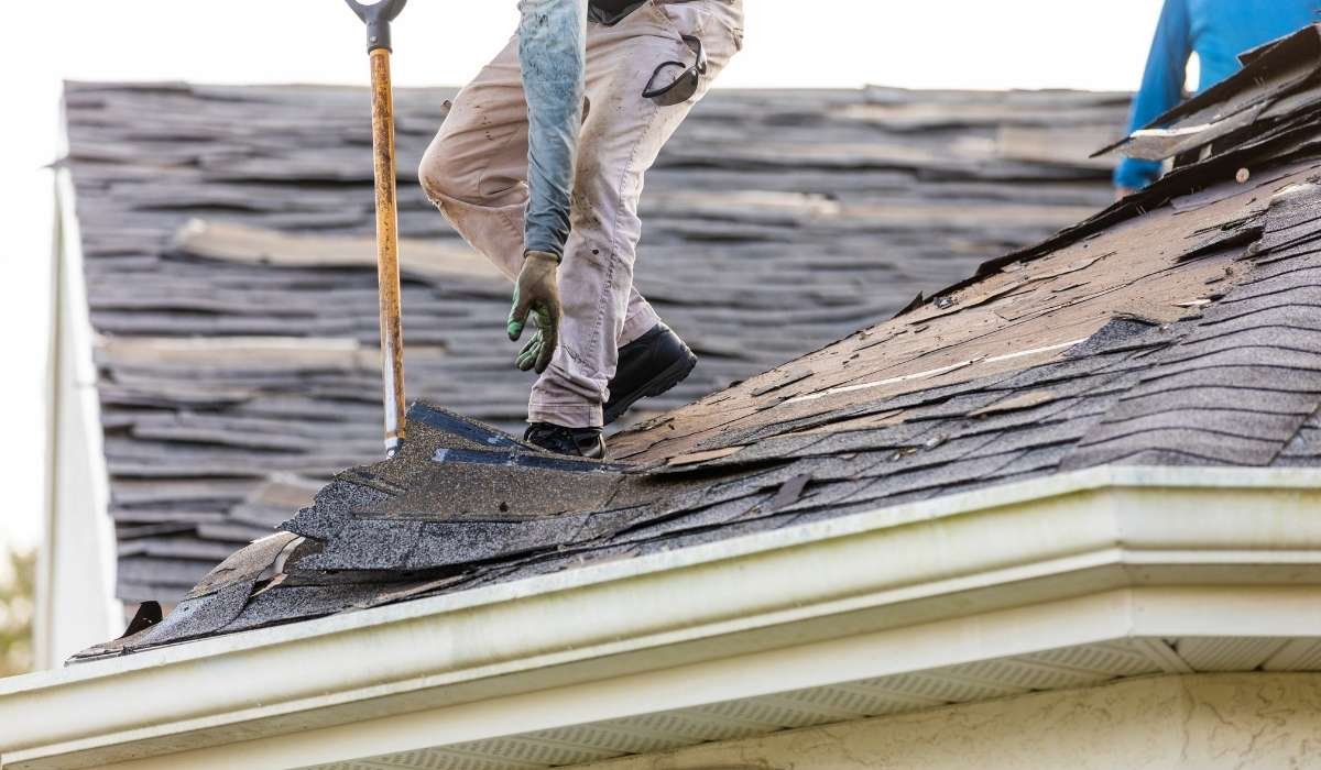 Roofer securing storm-damaged shingles on a residential home after heavy wind and rain